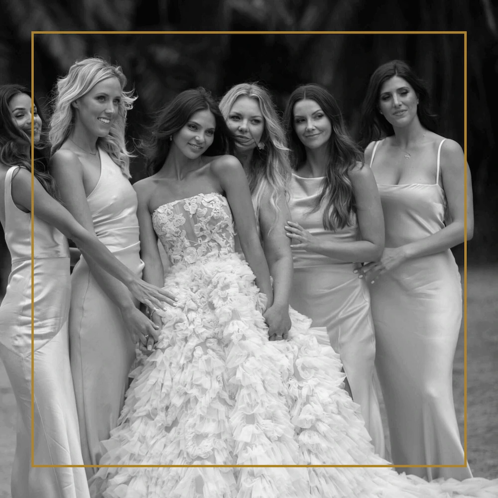 Bride in a feathered gown poses outdoors with bridesmaids in satin dresses.