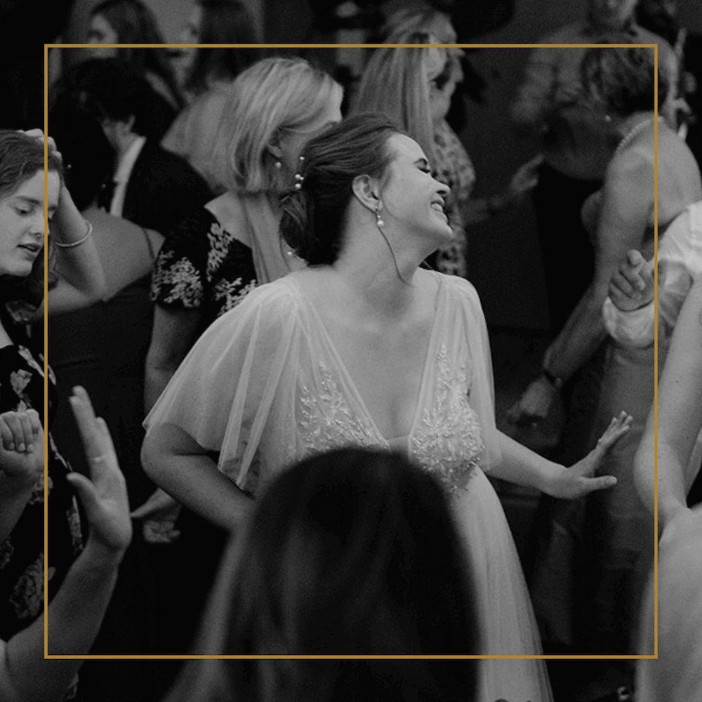 Bride laughing and dancing among a lively crowd at a wedding reception.