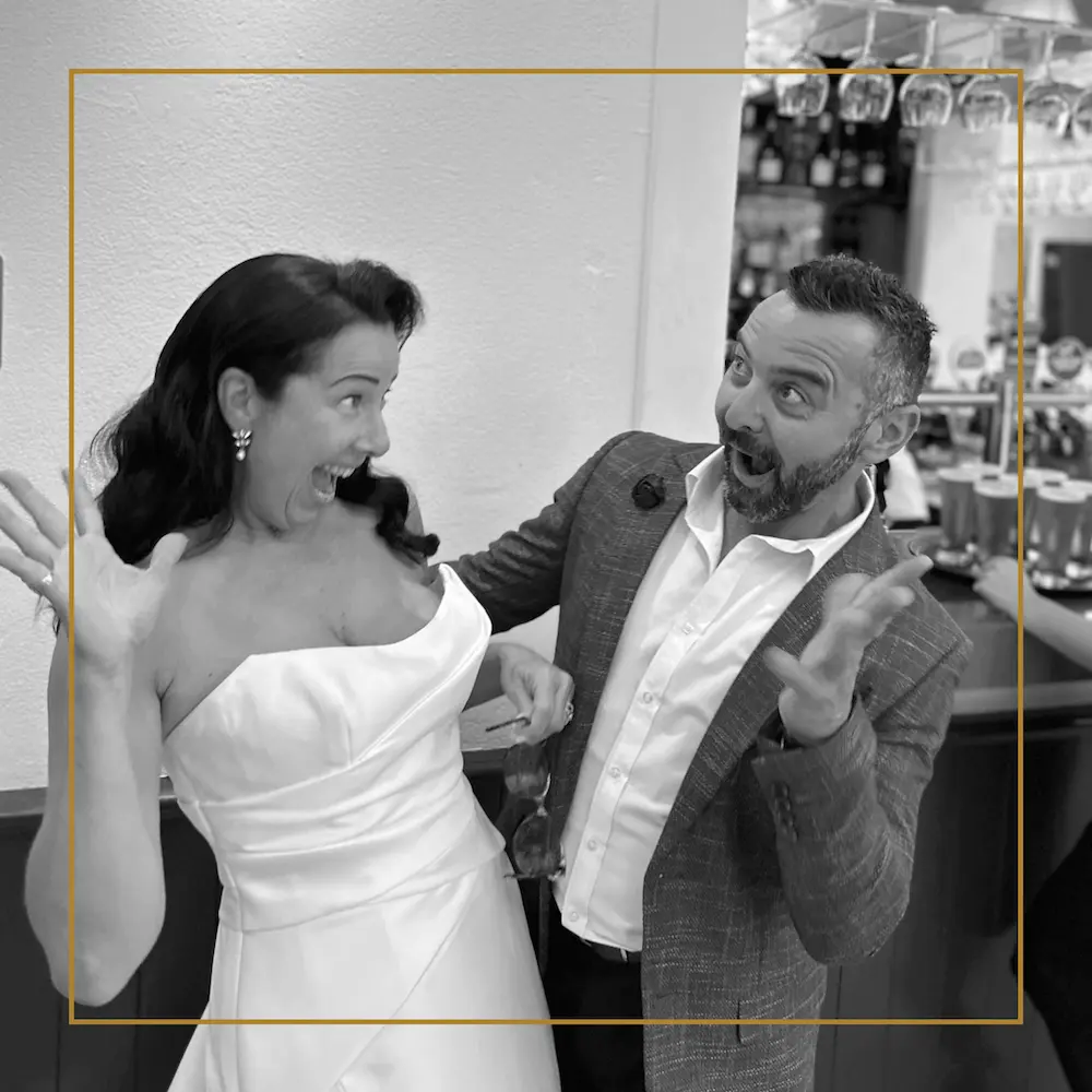 Bride and guest laughing with playful surprise expressions at a wedding reception.