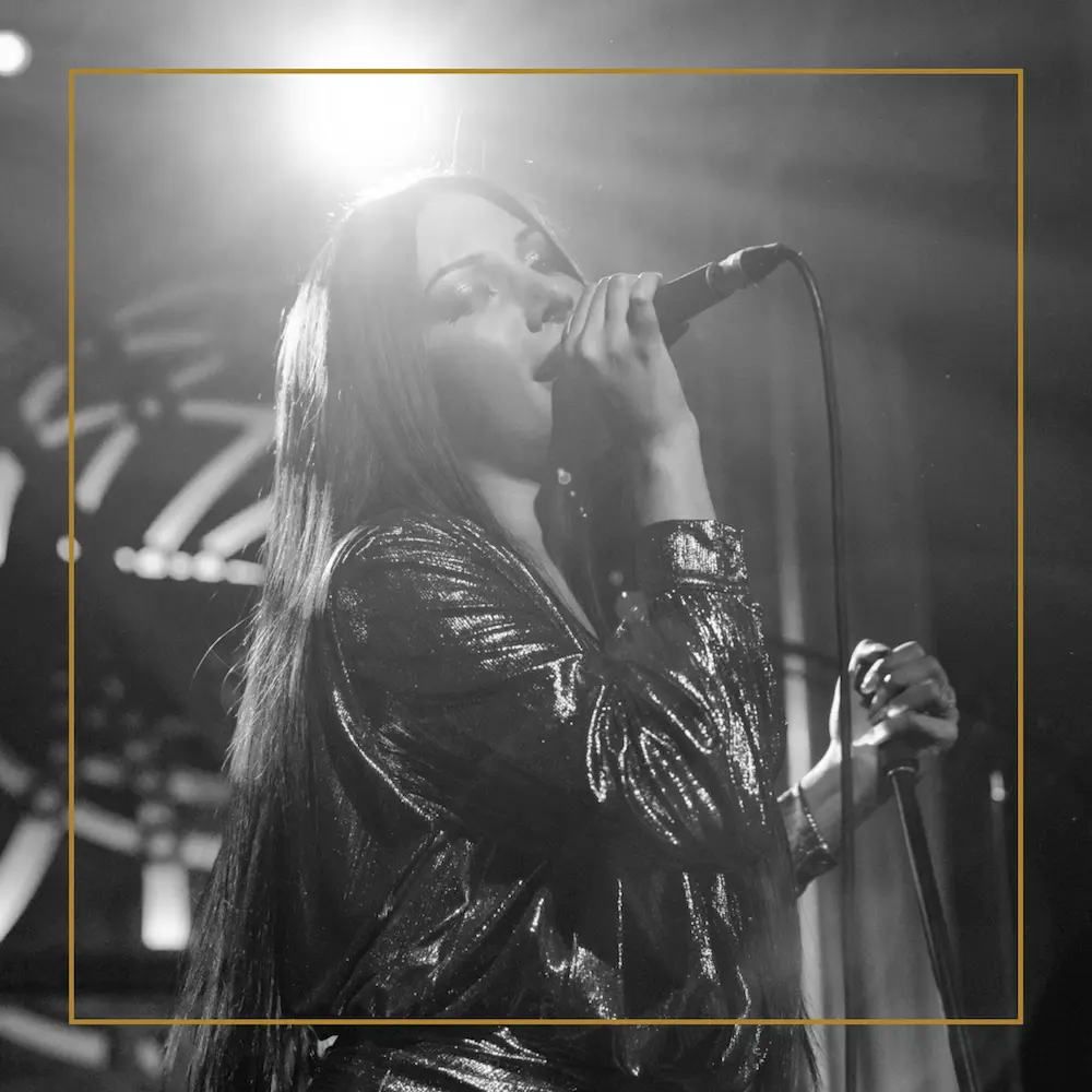Zandra performing on stage in a glittering outfit, singing into a microphone under bright lights.