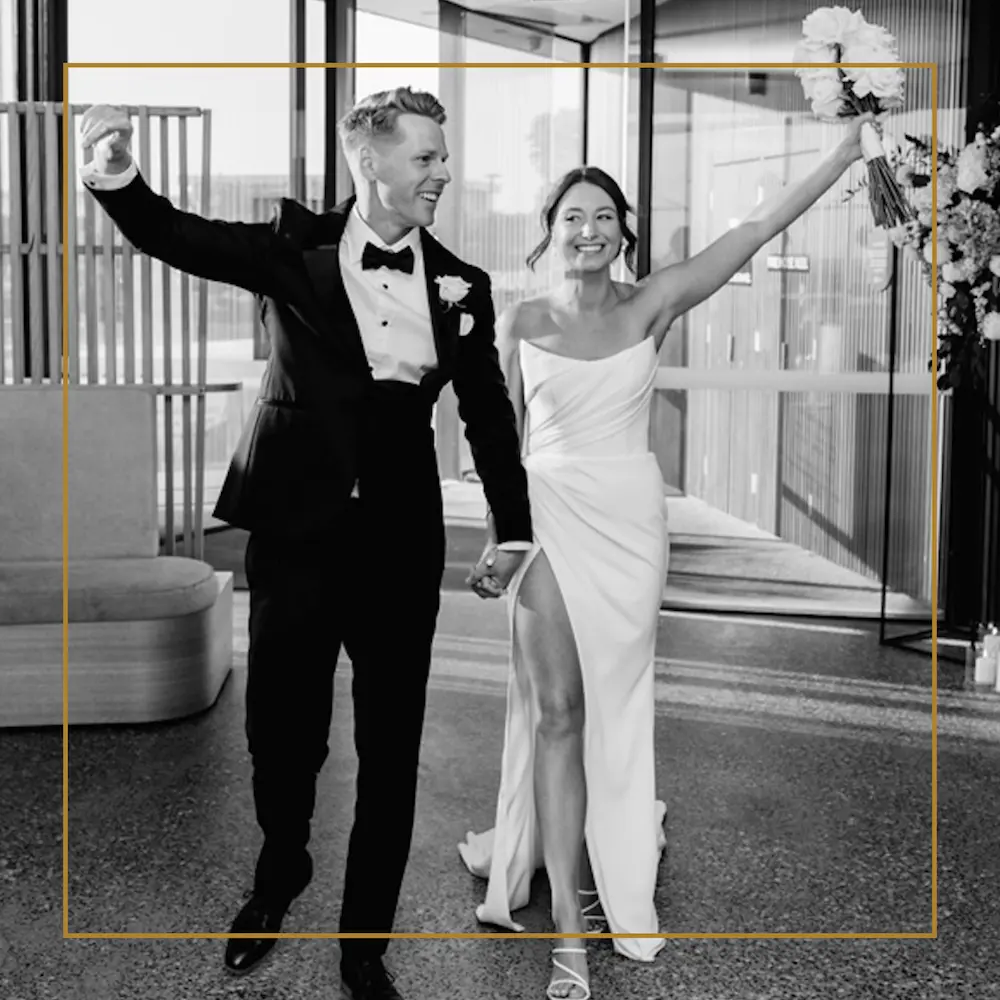 Bride and groom walk hand in hand, smiling and raising their arms in celebration after the wedding ceremony.